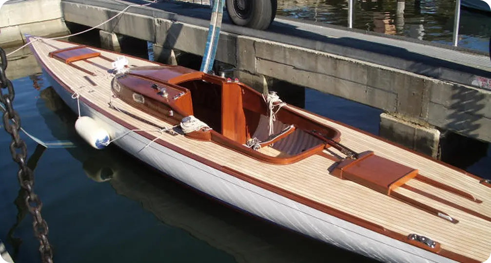 A sleek wooden boat with polished wood trim and two seats is moored at a marina. Reminiscent of classic Skerry Cruisers, oars rest across the deck, and the boat is secured to the pier with ropes. The water is calm and reflective.