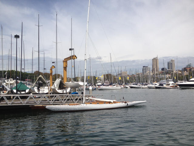 A marina filled with numerous Classic Sailing Yachts and sleek Schärenkreuzer moored at piers, with a cityscape and tall buildings visible in the background under a partly cloudy sky.