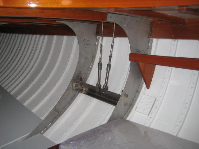 Interior view of a Schärenkreuzer boat hull showing white ribbed structure, metal reinforcement with bolts, tension cables, and polished wooden beams at the top—a fine example of Classic Sailing Yachts by Square Metre Yachts.