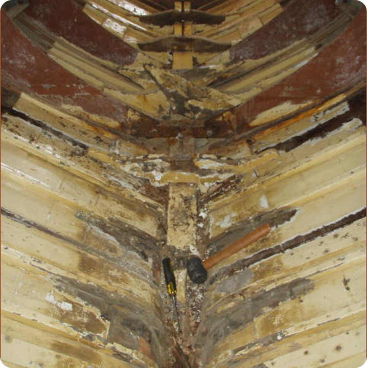 Close-up view of the inside hull of a Classic Sailing Yacht under repair, showing exposed ribs and weathered wood with a screwdriver and a handled tool lying in the centre.