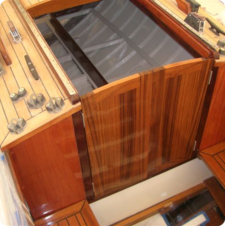 Wooden hatchway entrance with sliding doors leading below deck on a Schärenkreuzer, surrounded by polished wood surfaces, fittings, and controls. The area appears clean and well-maintained.