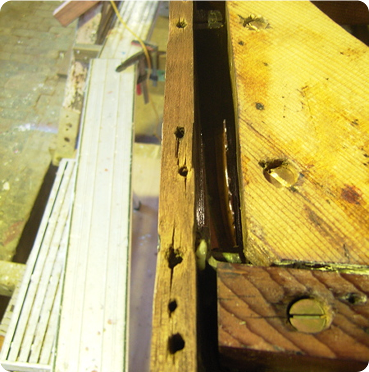 Close-up of two wooden planks joined together, one with several drilled holes along the edge, resting on a workbench—evoking the craftsmanship found in Classic Sailing Yachts, with wood shavings and tools in the background.