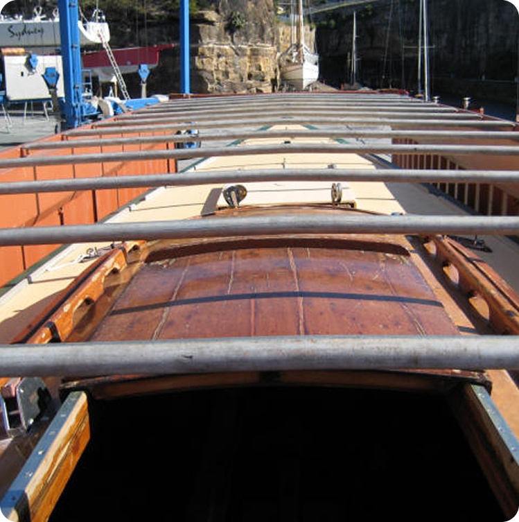 View from the deck of a wooden boat, looking forward past metal railings, with a classic Skerry Cruiser and dock structures visible in the background.
