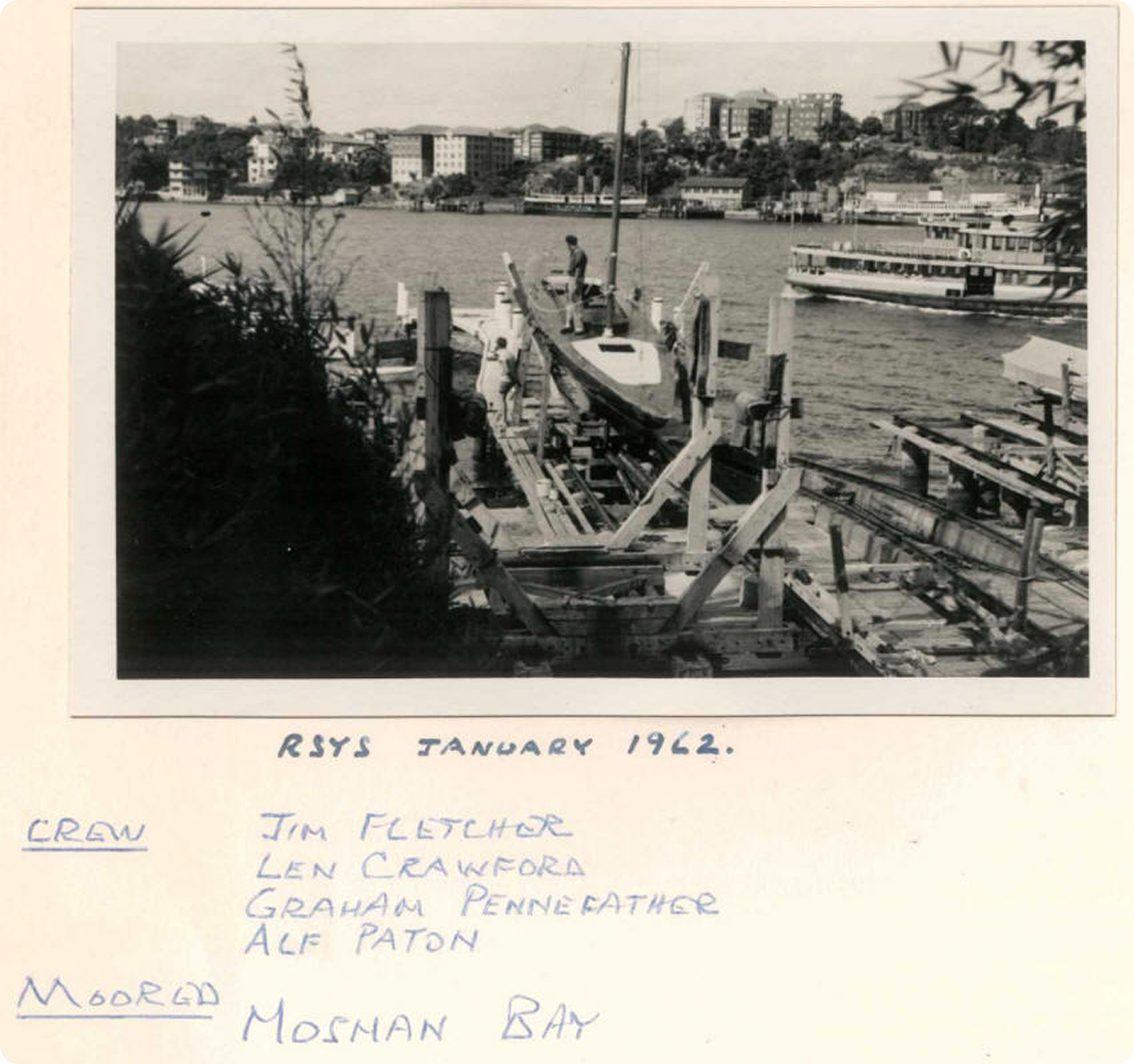 Black-and-white photo of a wooden jetty under construction by a bay, with Classic Sailing Yachts and buildings in the background. Handwritten names and the text “RSYS January 1962, Crew, and Moored Mosman Bay” appear below the image.