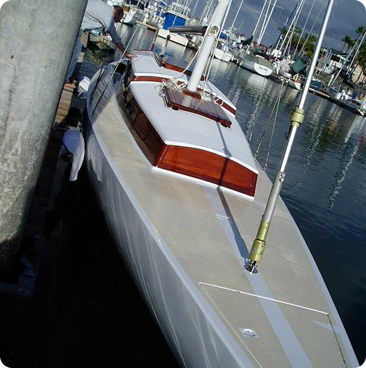 A sleek white Classic Sailing Yacht with wooden trim is moored at a marina, surrounded by other boats and calm water. A person is seen on the quay beside the boat.