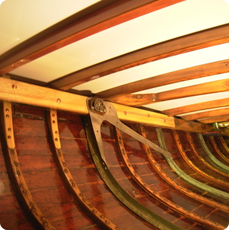 Interior view of a wooden boat showing curved ribs, wooden planks, and structural supports, highlighting craftsmanship and joinery details typical of Classic Sailing Yachts and Schärenkreuzer designs.