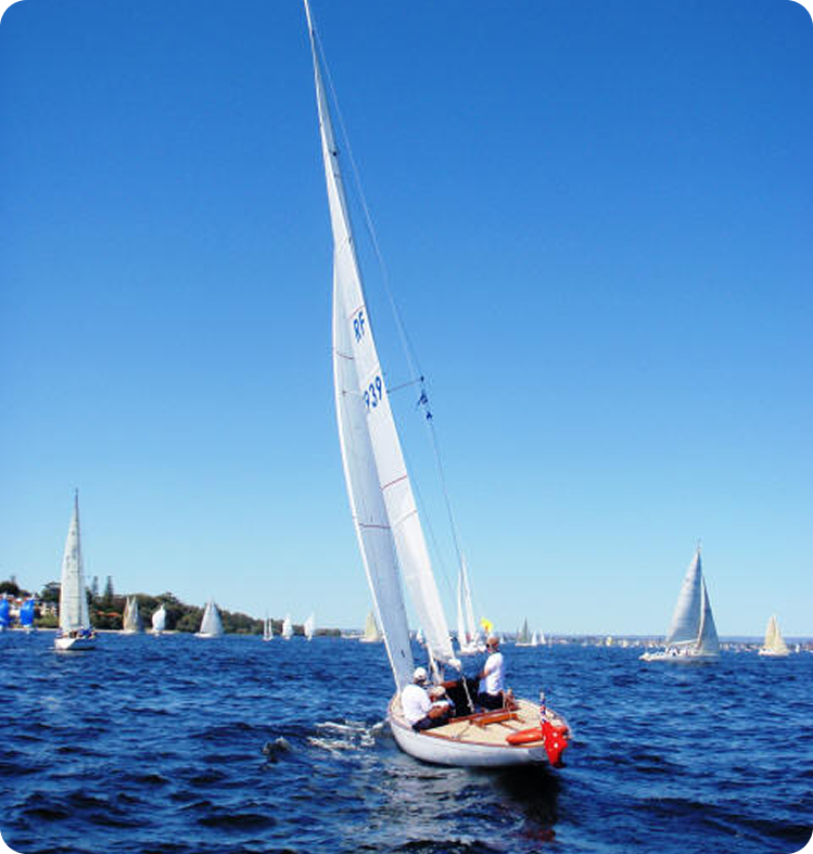 A classic sailing yacht with three people on board glides over blue water on a sunny day, surrounded by several other Square Metre Yachts under a clear blue sky.