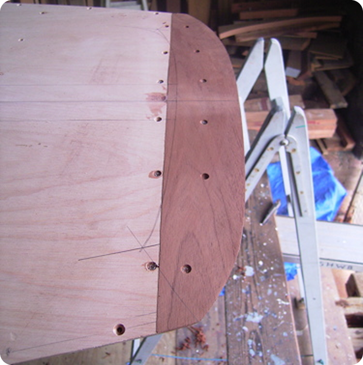 A close-up of two pieces of wood joined with screws, showing precise alignment and pencil markings on the lighter wood, set on a workbench in a workshop where Classic Sailing Yachts like Schärenkreuzer are crafted.