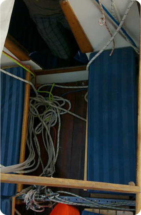 View of a Skerry Cruiser cabin interior with blue-striped cushioned seats and several coiled ropes on a wooden floor; part of a person is visible near the top left of the image.