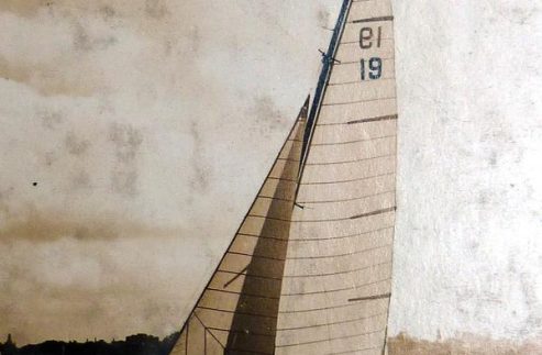 Sepia-toned photo of a Schärenkreuzer sailboat with two sails, bearing the number 19, gliding on the water—a classic sailing yacht silhouette against a distant shoreline and cloudy sky.
