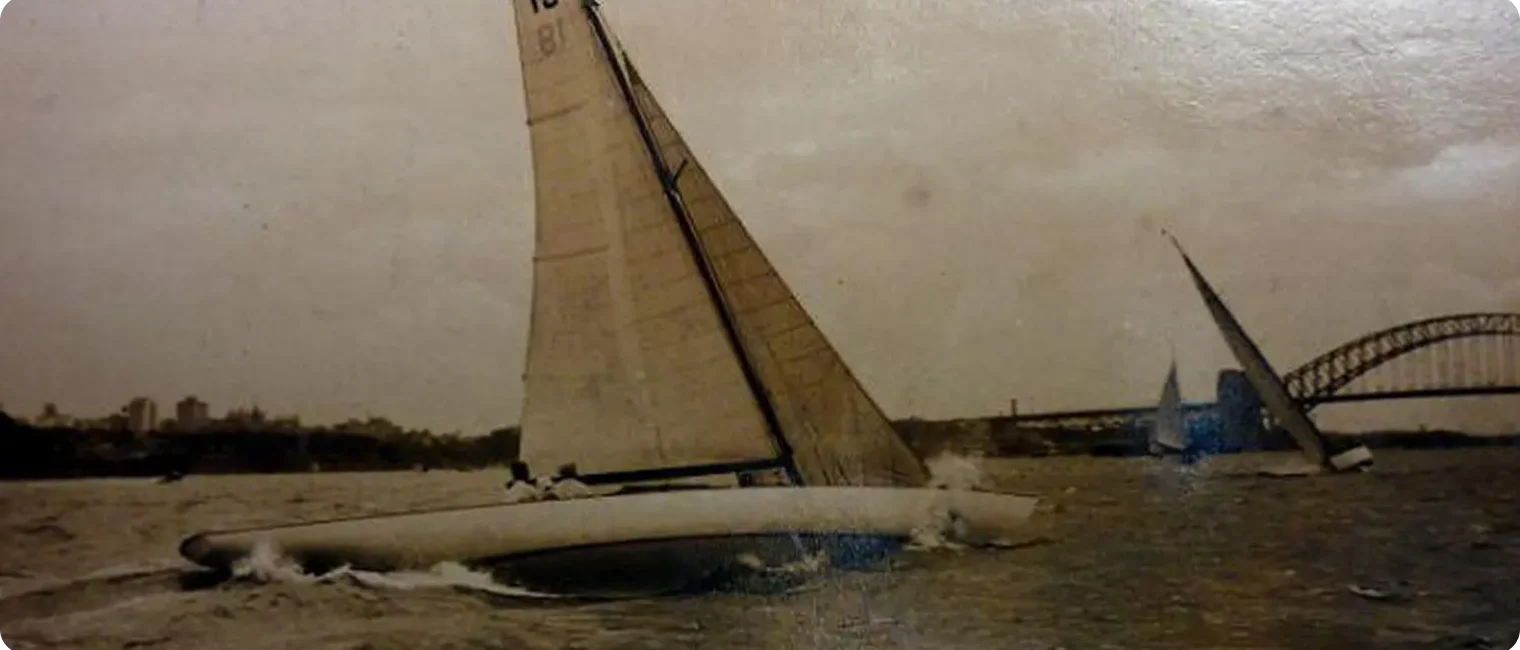 Sepia-toned photo of two Classic Sailing Yachts racing on choppy water with the Sydney Harbour Bridge visible in the background under a cloudy sky.