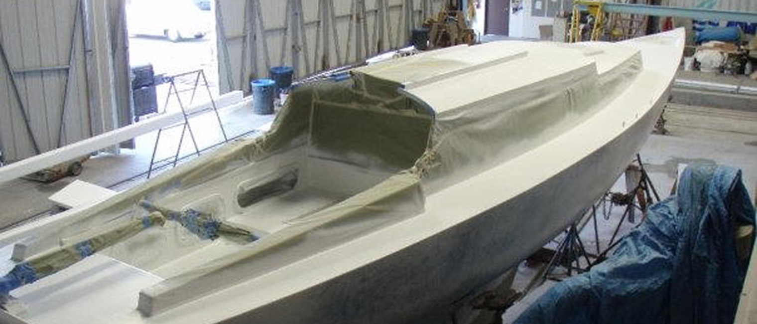 A Square Metre Yacht under construction or repair inside a workshop, with masking tape and protective covering around the cockpit area, and tools and equipment visible nearby.